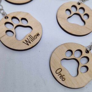 Porte-clés en bois clair en forme de disque,avec une découpe en forme d’empreinte de patte d’animal au centre. Les porte-clés sont reliés à des anneaux métalliques argentés.